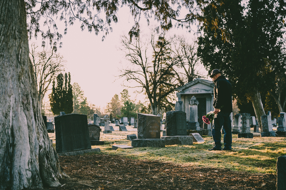 man standing alone in a cemetery with flowers