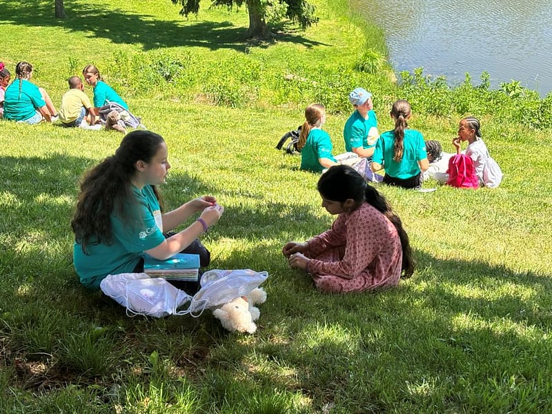 teen student sharing the gospel with a child on a grassy hill w